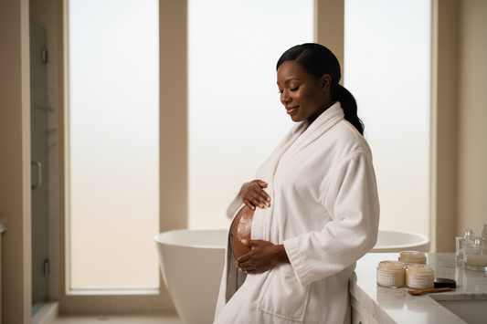  Pregnant Black woman applying body butter to baby bump with clean glass jars on marble countertop